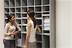 Colleagues chatting in front of filing shelves in office