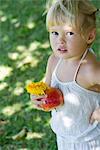 Little girl standing outdoors, holding apple and flower