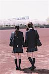 Japanese schoolgirls in their uniforms holding hands while walking away