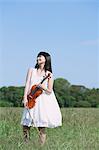 Femme asiatique avec un violon dans un champ d'herbe