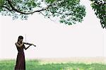 Asian woman playing the violin in a grass field