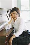 Japanese woman in a white shirt sitting by the piano and looking at camera