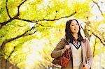 Japanische Frau mit langem Haar, Blick in die Kamera mit gelben Blättern im Hintergrund