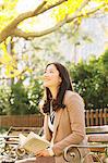 Japanese woman with long hair sitting on a bench in a park holding a book