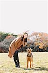 Japanische Frau mit langen Haaren und einem Hund in einem Park, Blick in die Kamera