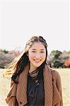 Porträt einer japanischen Frau mit langen Haaren in einem Park lächelnd in die Kamera