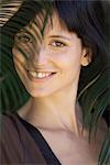 Young woman looking through palm leaf, smiling, portrait