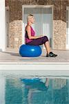 Jeune femme assise sur le ballon de fitness à la piscine