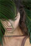Young woman behind palm frond, looking down sadly