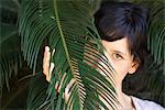 Jeune femme à la recherche par le biais de feuilles de palmier, portrait