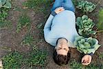 Man lying on ground, arm around cabbage plant, directly above