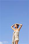 Mdi-adult woman standing wrapped in towel against blue sky, hands on head
