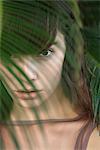 Young woman behind palm frond, portrait