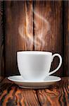 White cup with steaming hot drink on a wooden background