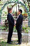 Handsome gay couple holding hands under their floral wedding arch.