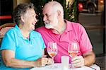 Senior couple flirting and laughing together over a glass of white wine.