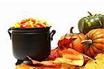 A cauldron of candy corn next to pumkins and leaves.