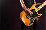 Photo of the body of a female guitar player standing and playing over a dark background.