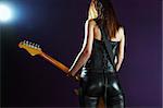 Foto von der Rückseite des weiblichen Gitarrist stehen und vor einen Scheinwerfer zu spielen.