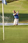 Senior Male Golfer Playing Bunker Shot On Golf Course