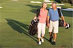 Senior Couple Walking Along Golf Course Carrying Bags