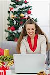 Heureuse jeune femme près d'arbre de Noël à l'aide d'ordinateur portable