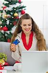 Happy young woman near Christmas tree making online purchases