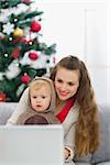 Mother and baby near Christmas tree using laptop