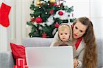 Surprised mother and baby near Christmas tree looking in laptop