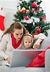 Mère montrant quelque chose dans l'ordinateur portable près de sapin de Noël de bébé