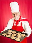 Handsome chef holding a plate of freshly baked chocolate chip cookies.  Red background.