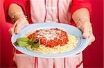 Closeup of mom's hands holding a plate of homemade spaghetti marinara.