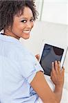 Belle heureuse jeune femme afro-américaine ou fille souriant et à l'aide d'une tablet PC à la maison sur son canapé