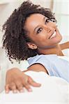 A beautiful mixed race African American girl or young woman sitting on sofa at home looking happy and relaxed