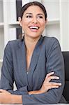 Beautiful happy young Latina Hispanic woman or businesswoman in smart business suit sitting at a desk in an office laughing