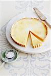 Lemon Tart on Marble Stand with Pie Server and Bowl of Icing Sugar on Table in Studio