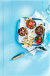 Gegrillte Burger und Pita-Brot auf Tablett mit Spachtel auf blau Holztisch im Studio