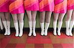 Waist Down View of Six Women Dressed in Vintage Pink Dresses and White Go-go Boots Standing in a Row on Checkered Floor