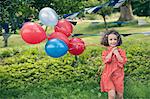 Girl holding bunch of balloons outdoors