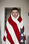 Boy wrapped in American flag indoors