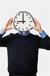 Young man covering his face with clock standing against white background