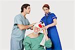 Male doctor with female nurse bandaging an injured patient against gray background