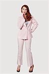 Beautiful young businesswoman in pink suit standing against gray background