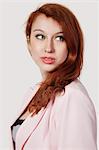 Beautiful young businesswoman in pink suit looking away against gray background