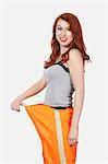 Portrait of young Caucasian woman oversized orange pants against gray background