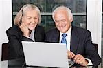 Couple heureux supérieurs d'entreprises regardant blanc ordinateur portable assis à table