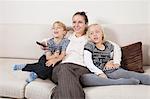 Heureuse jeune femme avec des enfants sur le canapé à regarder la télévision