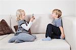 Young girl photographing brother through cell phone on sofa