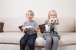 Happy brother and sister playing video game on sofa