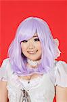 Portrait of cute young woman in doll costume and purple wig over red background